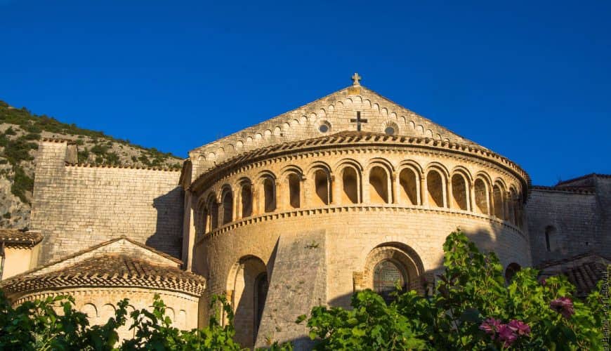 Bâtiment roman en pierre entouré de végétation sous un ciel bleu.