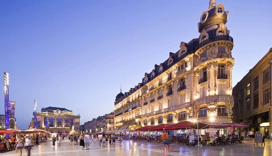 Place animée le soir, entourée de bâtiments historiques éclairés et de cafés.