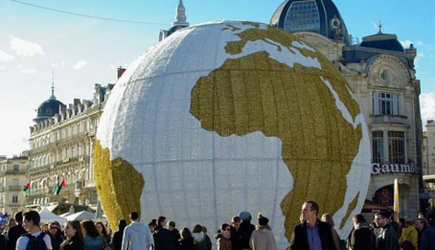 Grande sculpture d'un globe terrestre entourée de passants et de bâtiments historiques sur une place.