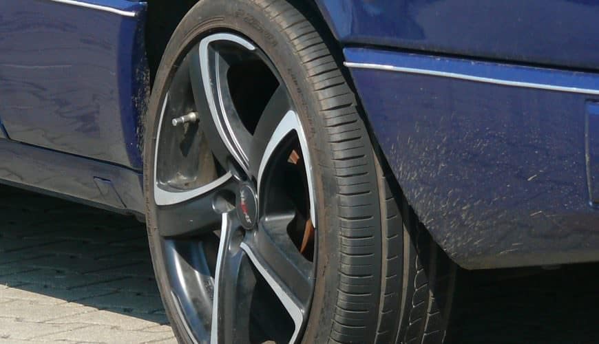 Voiture bleue stationnée avec un pneu crevé sur une surface pavée.