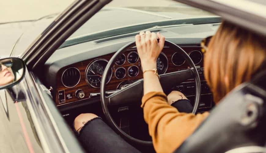 Personne au volant d'un classique, tableau de bord en bois, jean noir déchiré visible.