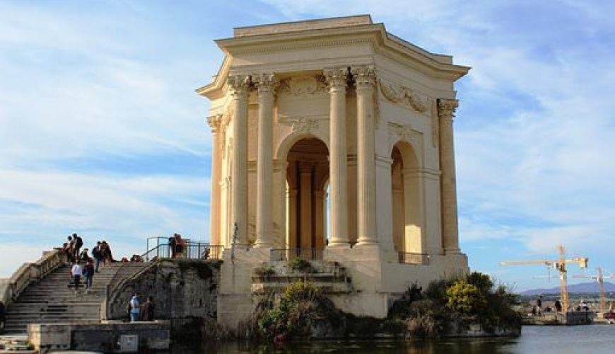 Monument néoclassique entouré d'eau avec colonnes, toit orné, proches d'un escalier.