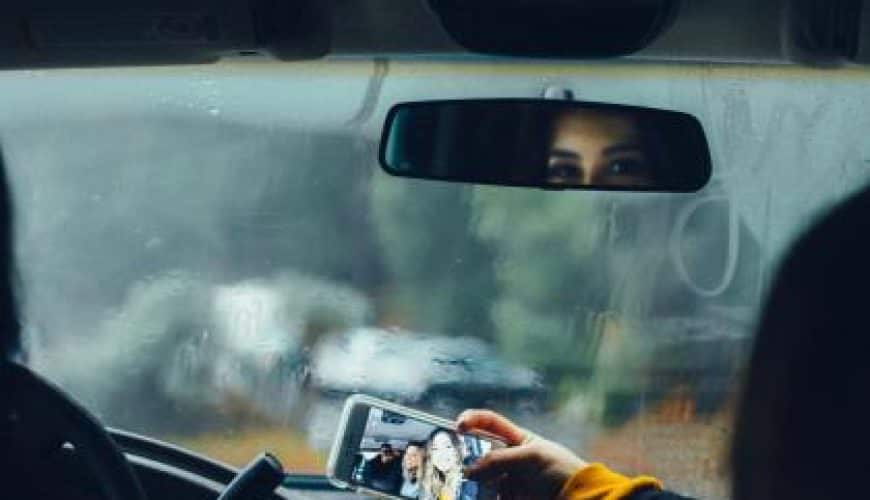 Personne utilise un smartphone pour prendre une photo dans une voiture, vitre embuée, reflet visible.