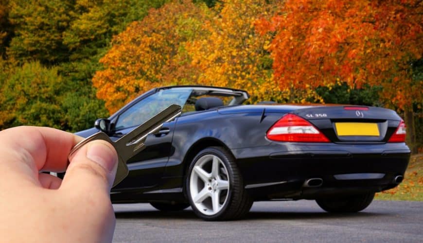 Main holding car key with convertible in autumnal background.