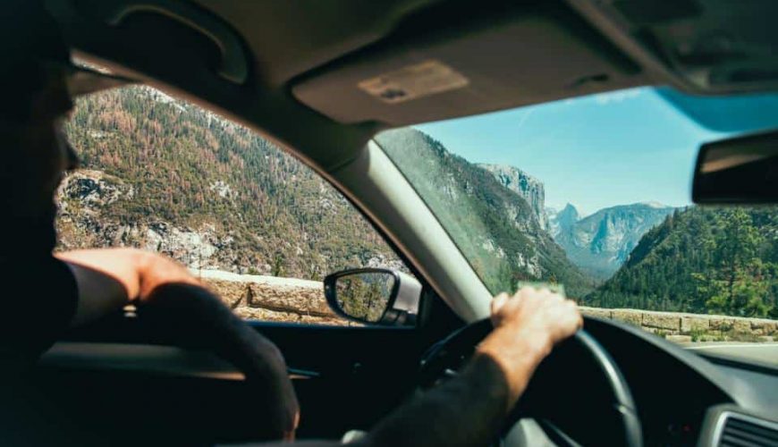 Conducteur dans une voiture sur route de montagne, vue panoramique sur vallées et sommets boisés.