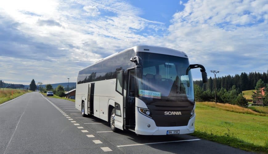 Autocar de tourisme blanc stationné sur route bordée de verdure, ciel partiellement nuageux.