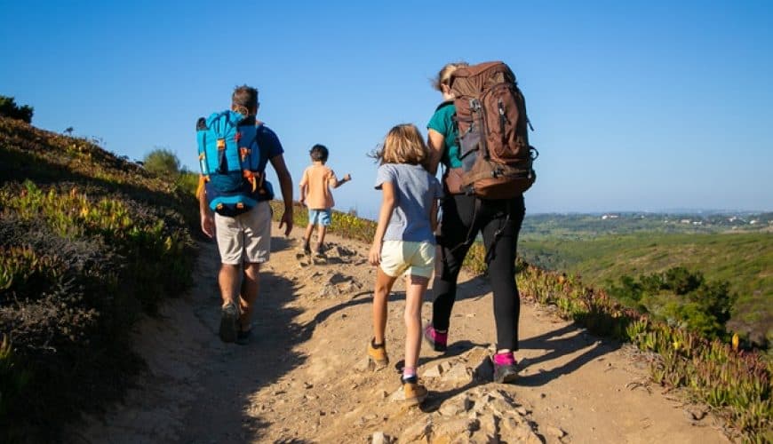 Famille en randonnée sur un sentier de montagne sous le soleil.