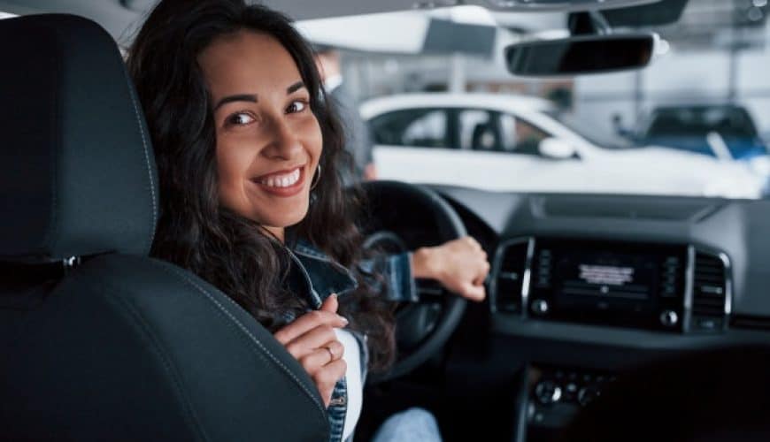 Femme souriante assise dans une voiture, regardant par-dessus son épaule.