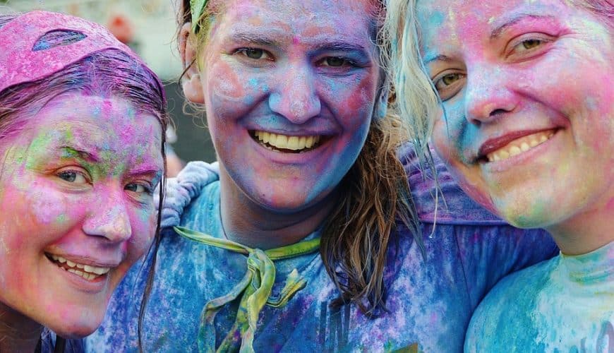 Trois personnes souriantes couvertes de poudre colorée lors d'un festival ou événement festif.