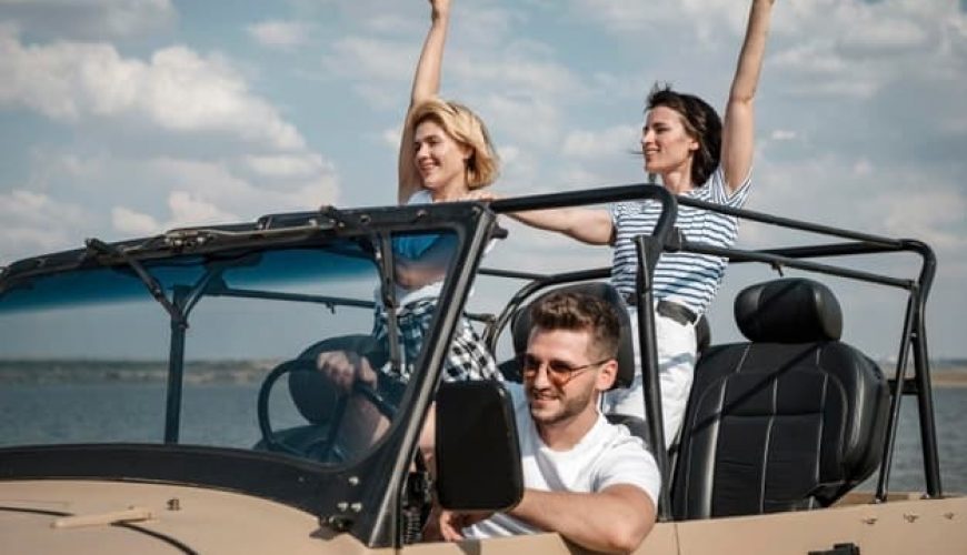 Trois personnes voyagent en décapotable près d'une étendue d'eau par jour ensoleillé.