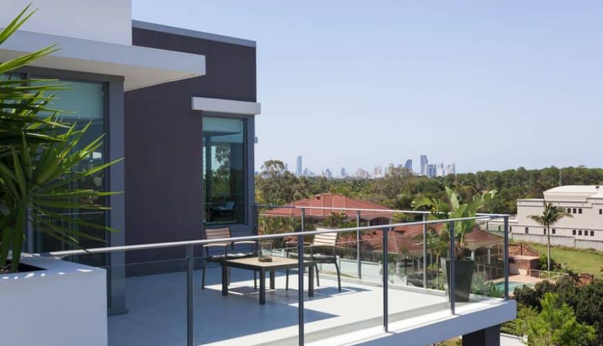 Terrasse moderne avec garde-corps en verre, vue sur la ville et plantes en pot.