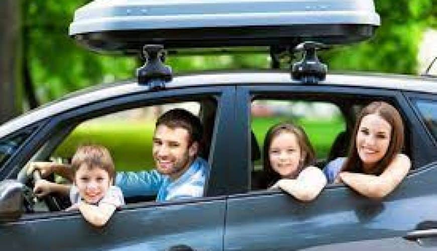 Famille de quatre personnes dans une voiture avec coffre de toit, prête pour un voyage.