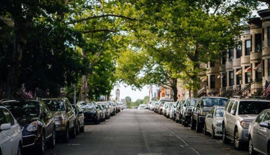 Rue bordée d'arbres avec voitures et bâtiments résidentiels en arrière-plan.