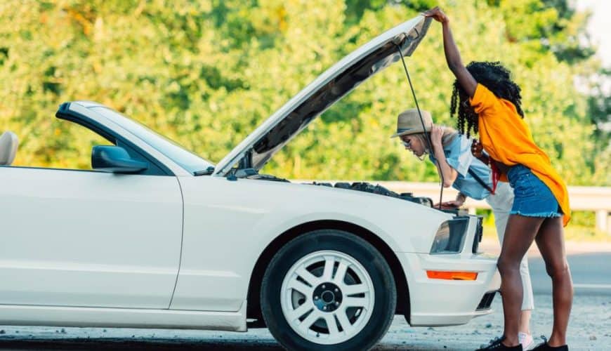 Deux personnes examinent le moteur d'une voiture décapotable blanche avec le capot ouvert.