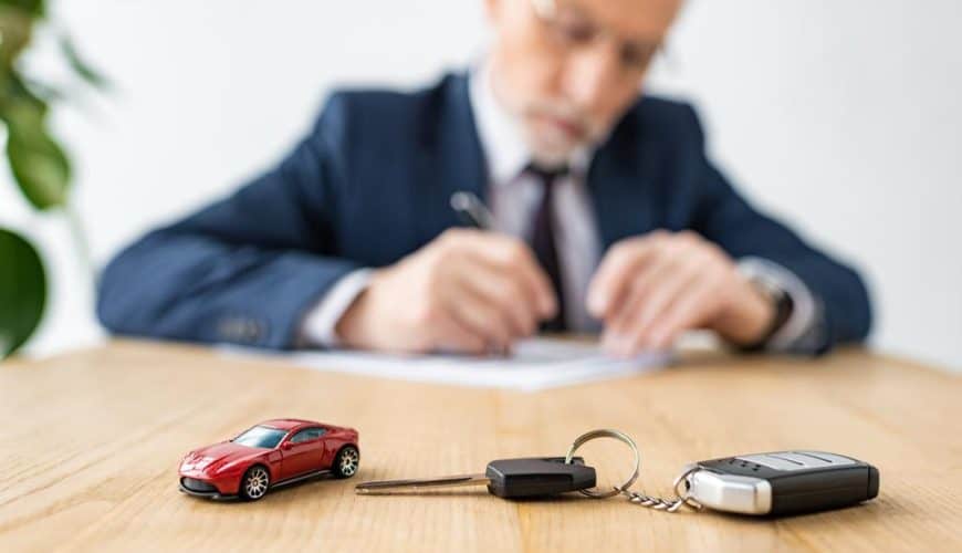 Homme en costume écrit, voiture rouge miniature et clé sur la table.