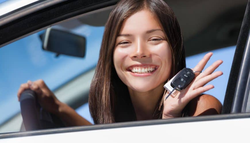 Personne souriante assise dans une voiture avec une clé de voiture à la main droite.