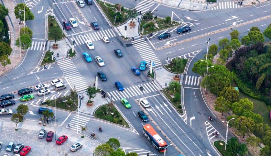 Carrefour urbain complexe avec voitures, bus, verdure et passages piétons.