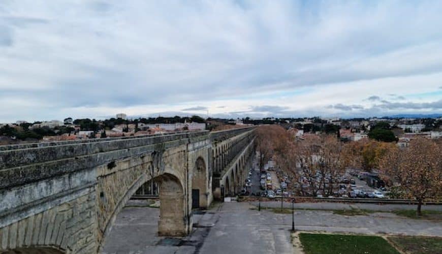 Aqueduc en pierre au-dessus d'une zone urbaine avec végétation et ciel couvert.