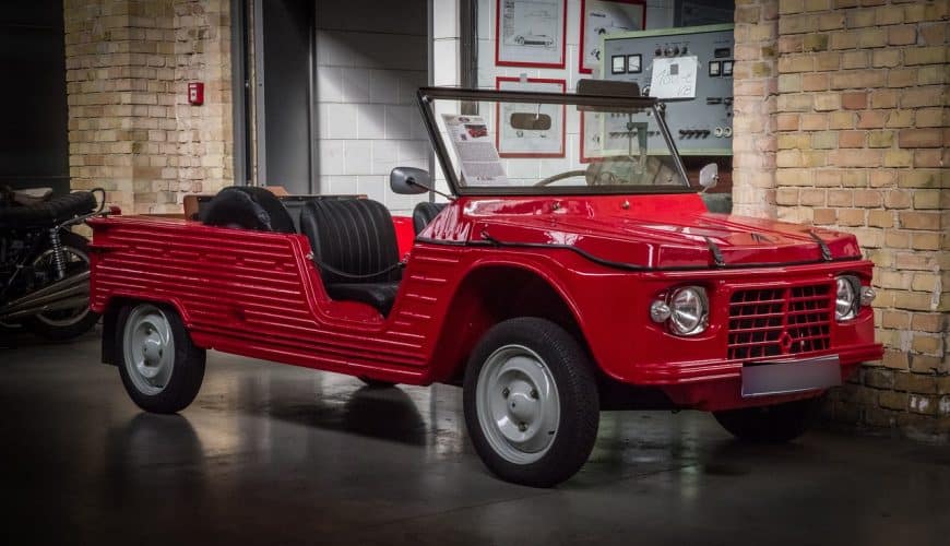 Retro red convertible car, two-seater, displayed indoors with wall-mounted equipment.