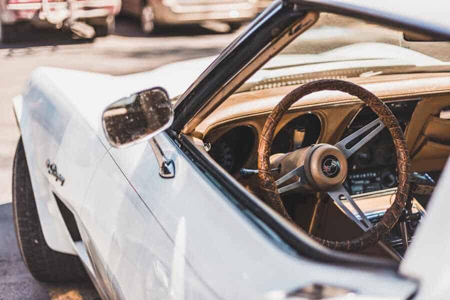 Voiture décapotable blanche avec intérieur cuir brun, volant et tableau de bord visibles.
