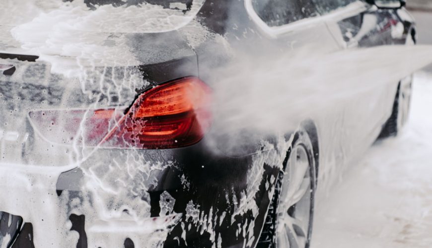 Car being washed with soapy foam, focusing on the rear with a visible red taillight.