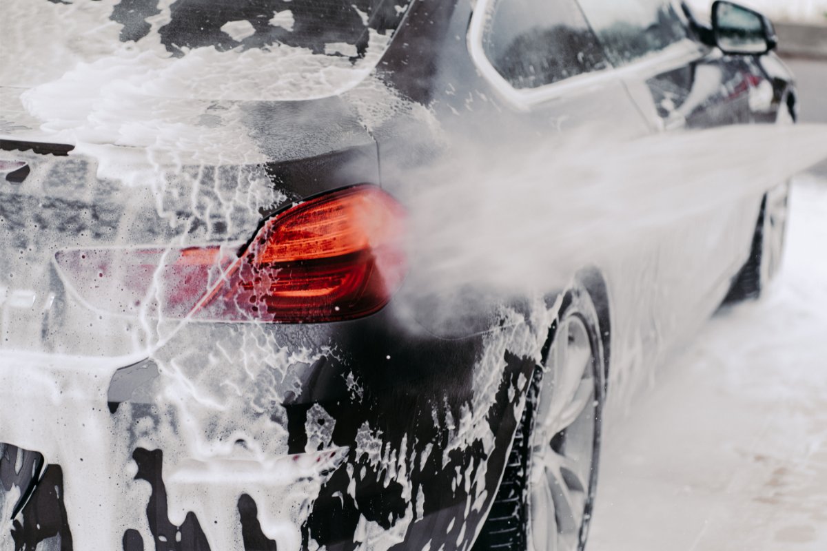 Car being washed with soapy foam, focusing on the rear with a visible red taillight.