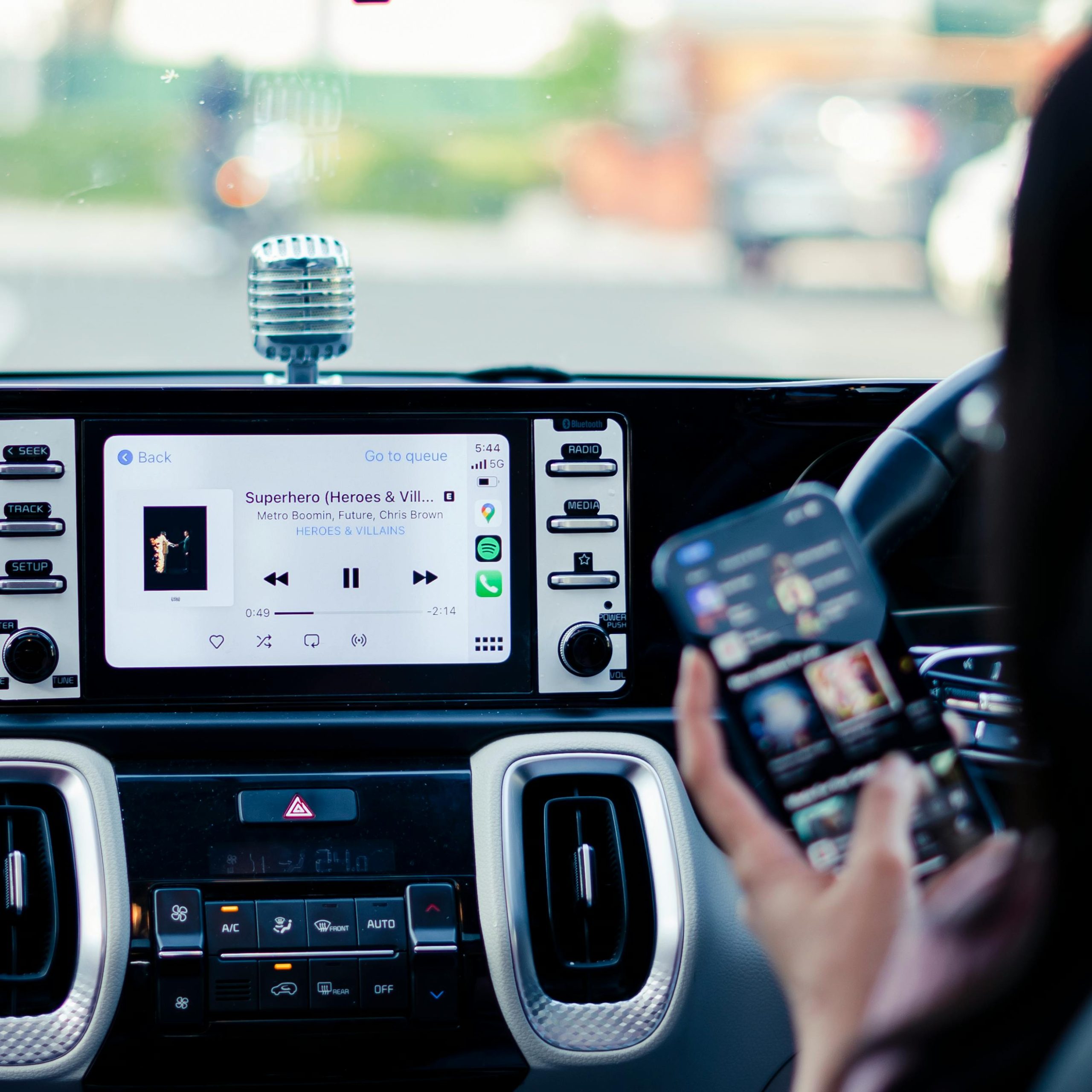 Tableau de bord de voiture avec écran musical et personne tenant un smartphone.